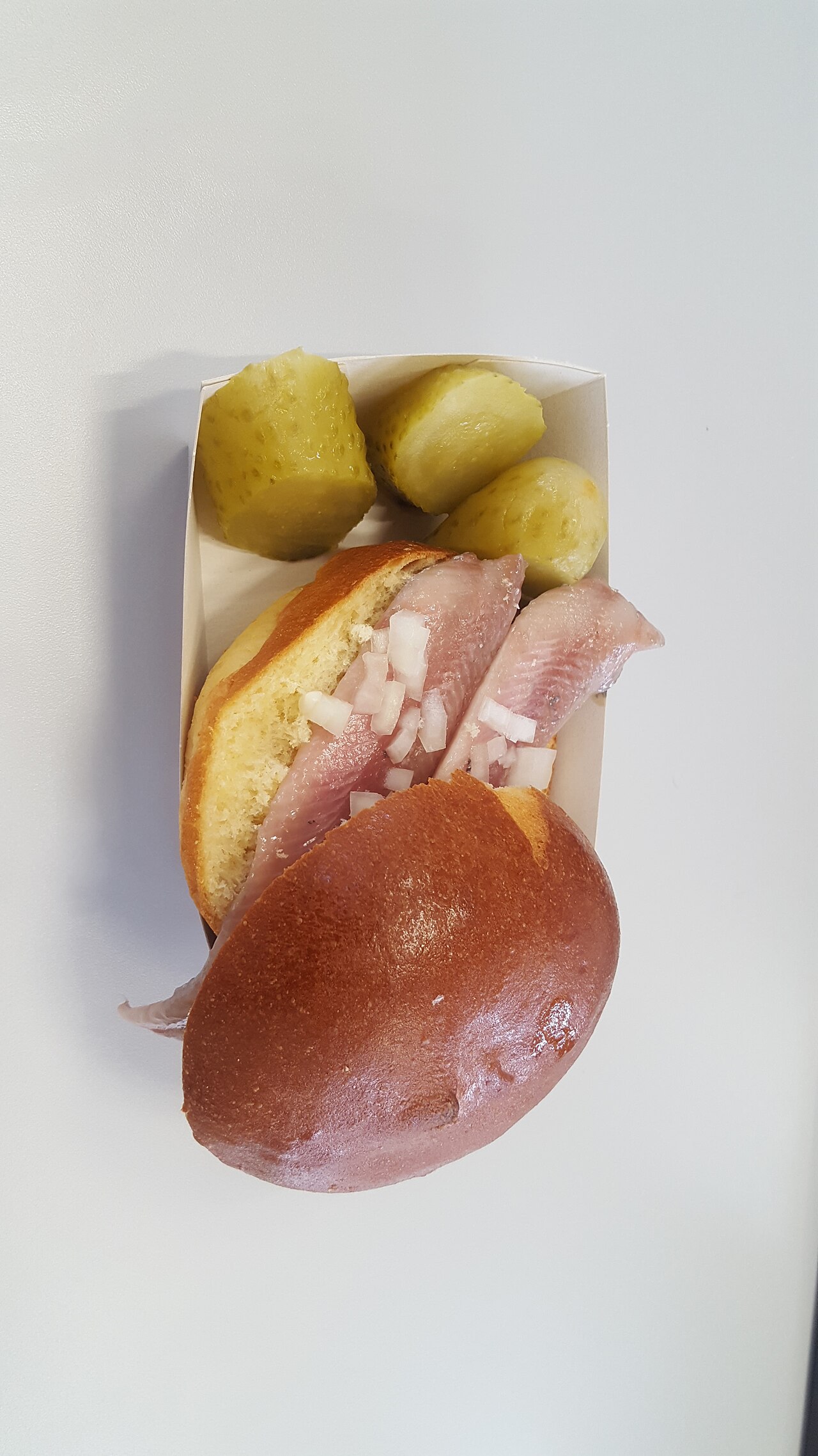 A broodje haring with chopped onion and pickles